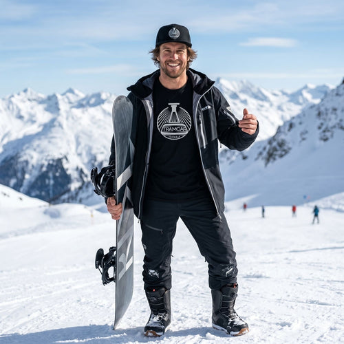 Person holding a snowboard with mountains in the background